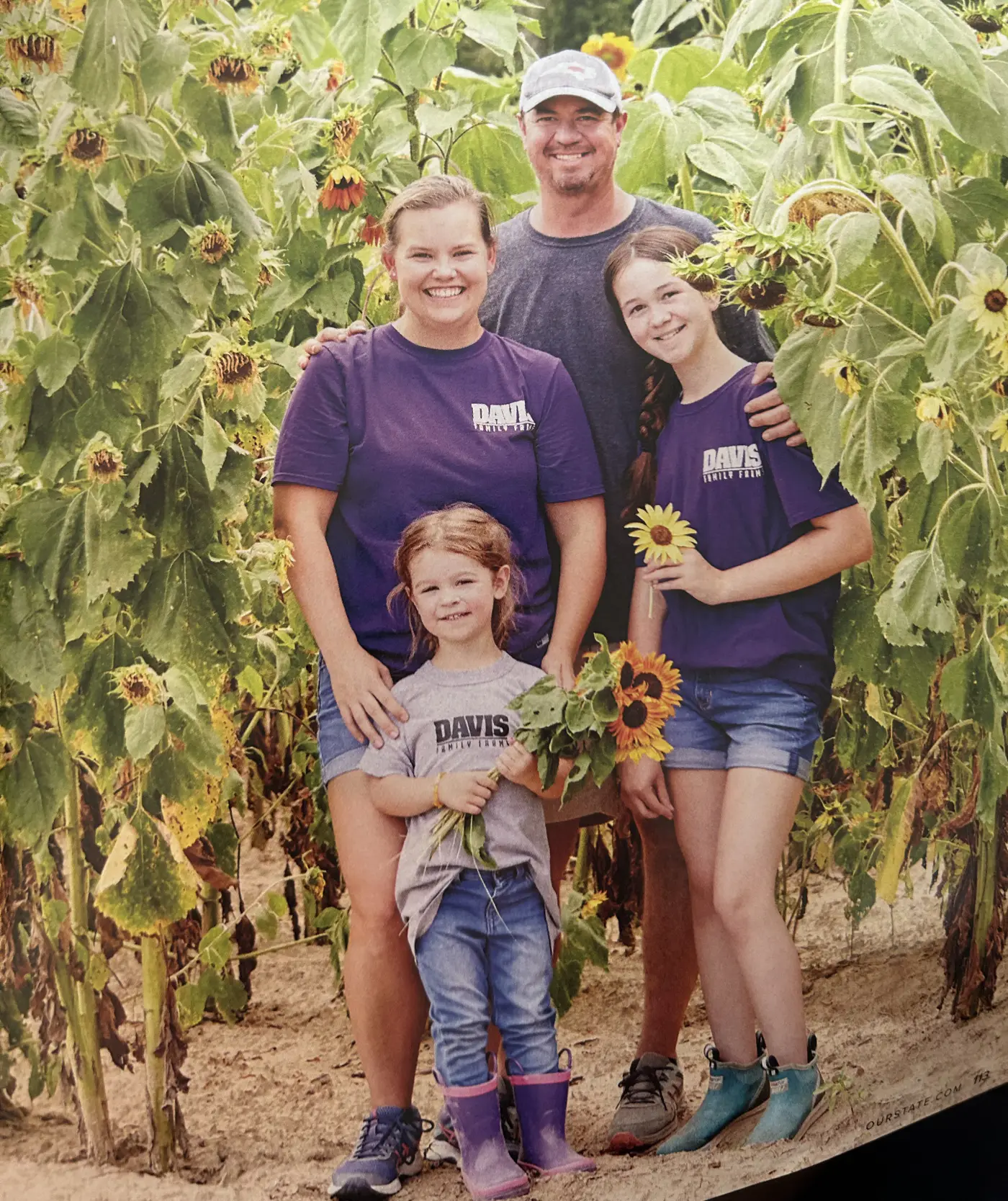 Josh and Erin Davis and their two daughters standing in a sunflower field in Davis Family Farms t-shirts
